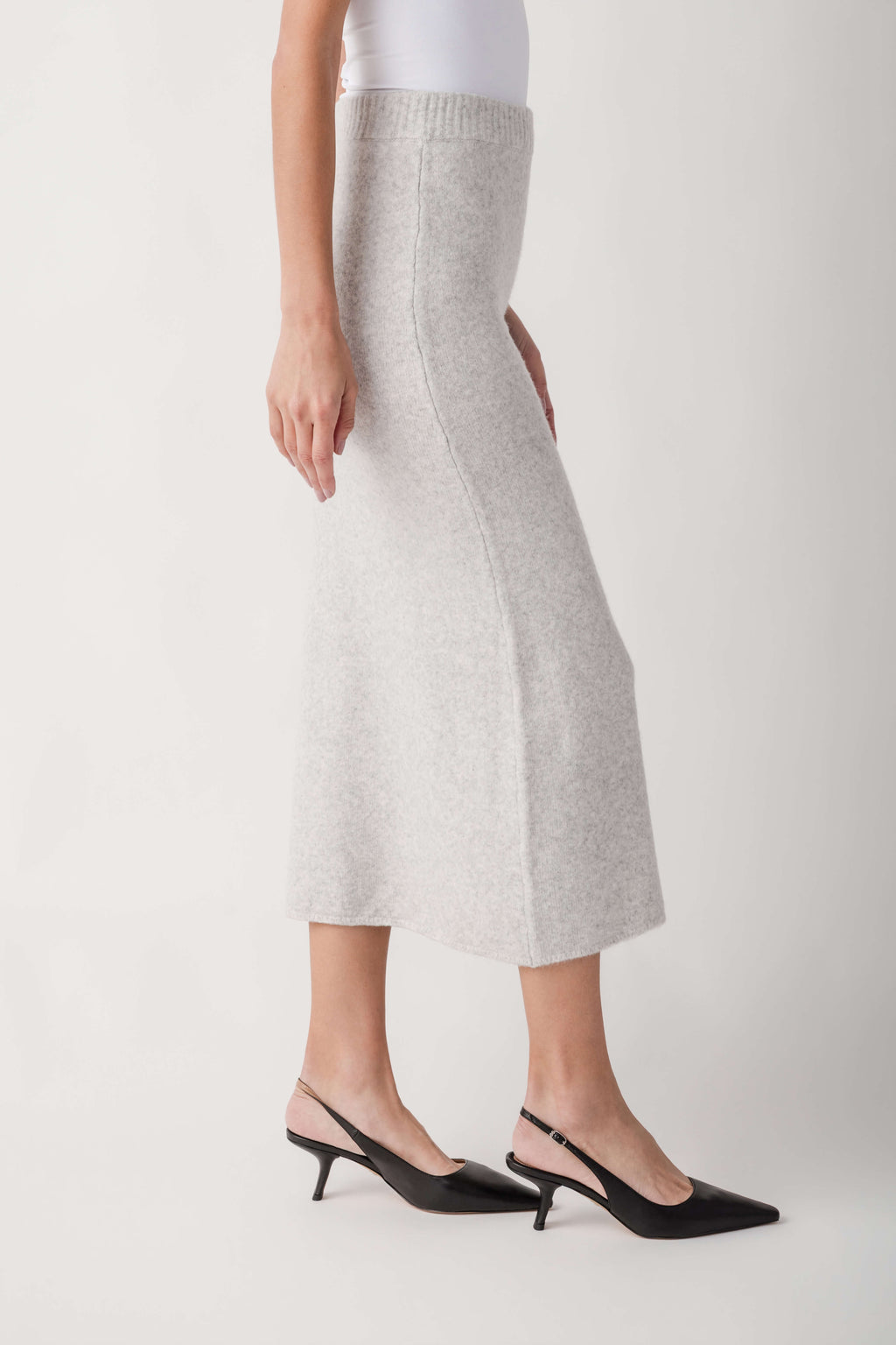 Light gray knit midi skirt with ribbed waistband worn with white top and black heels.