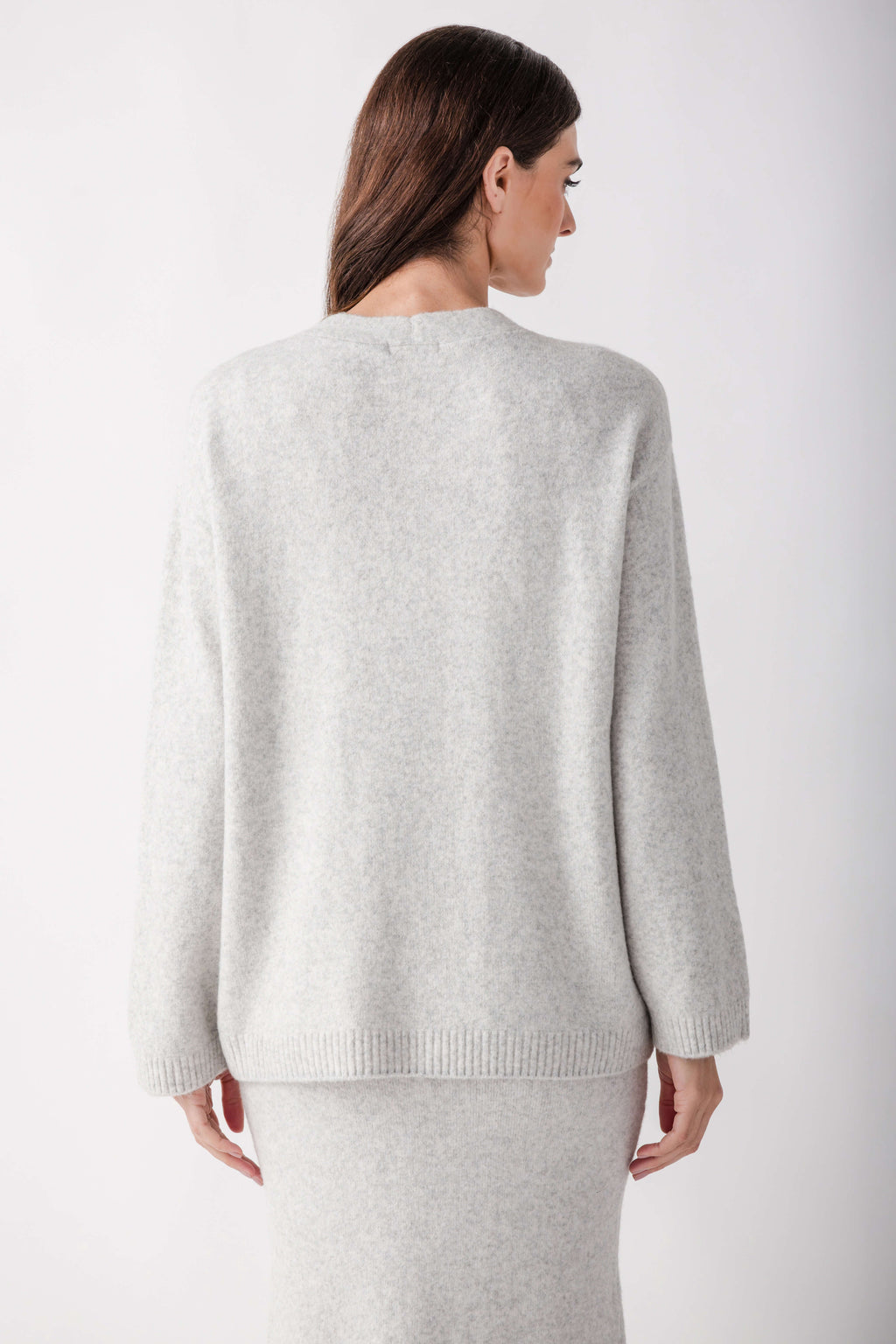Woman wearing a light gray knit cardigan with long sleeves, shown from the back.