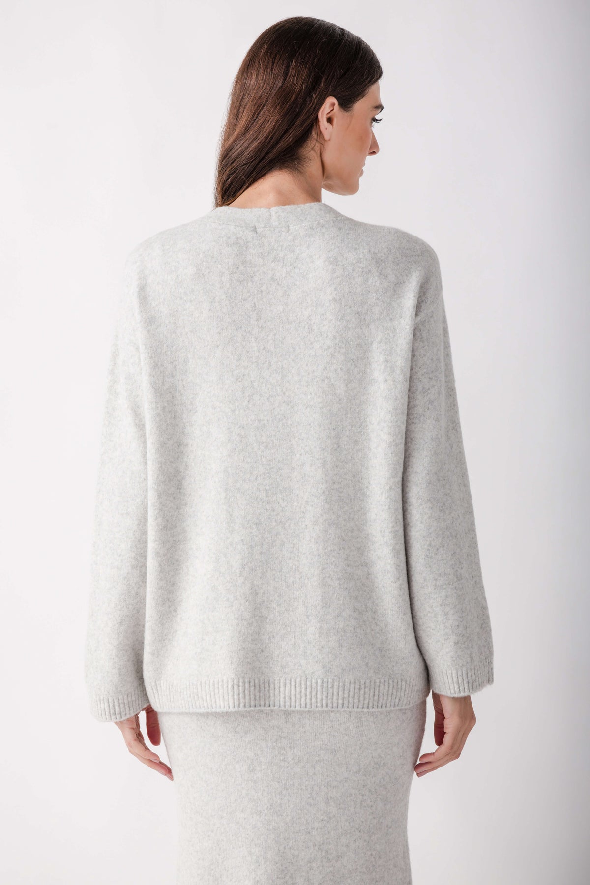 Woman wearing a light gray knit cardigan with long sleeves, shown from the back.