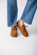 Tan suede loafer shoes with lace-up front and sherpa collar lining, worn with blue denim jeans.