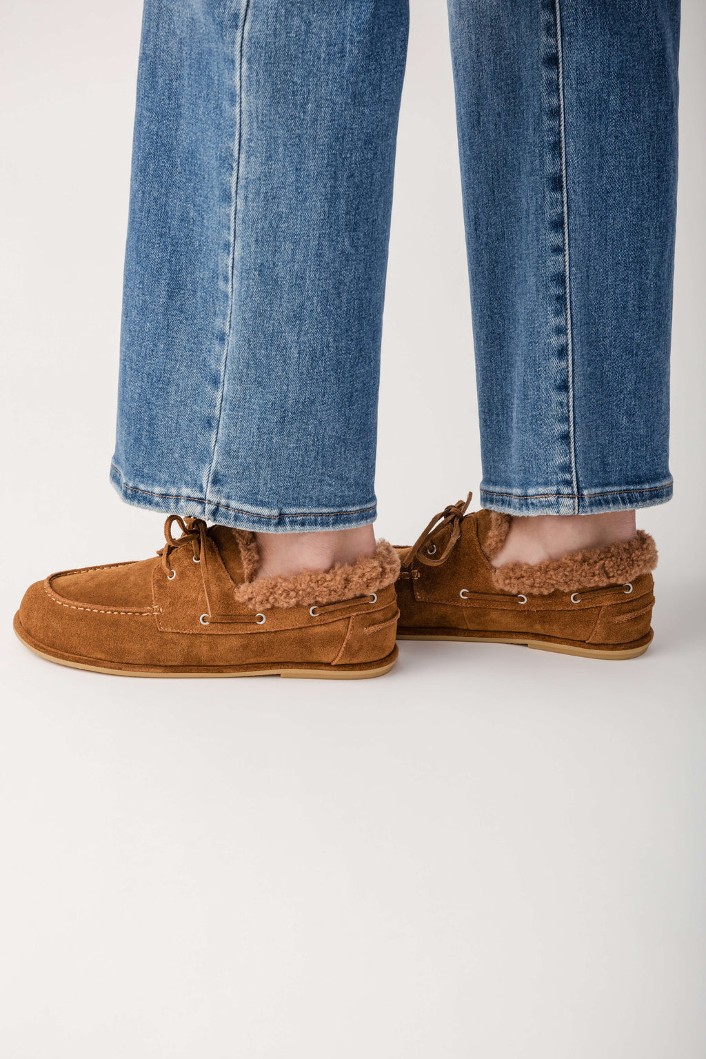 Tan suede boat shoe with sherpa lining and lace-up closure worn with blue jeans.