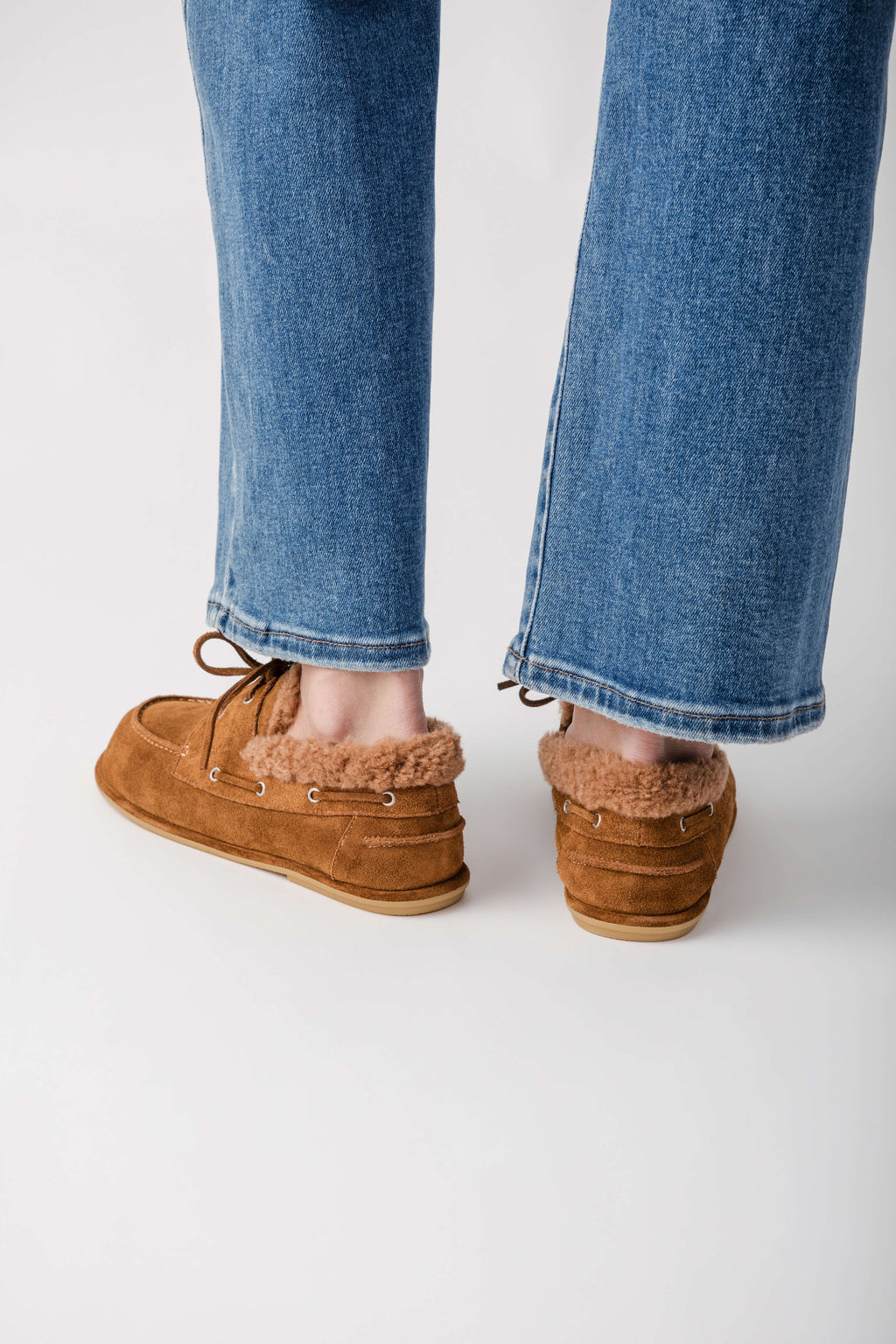 Tan suede moccasin with fuzzy lining and lace-up detail worn with blue jeans.