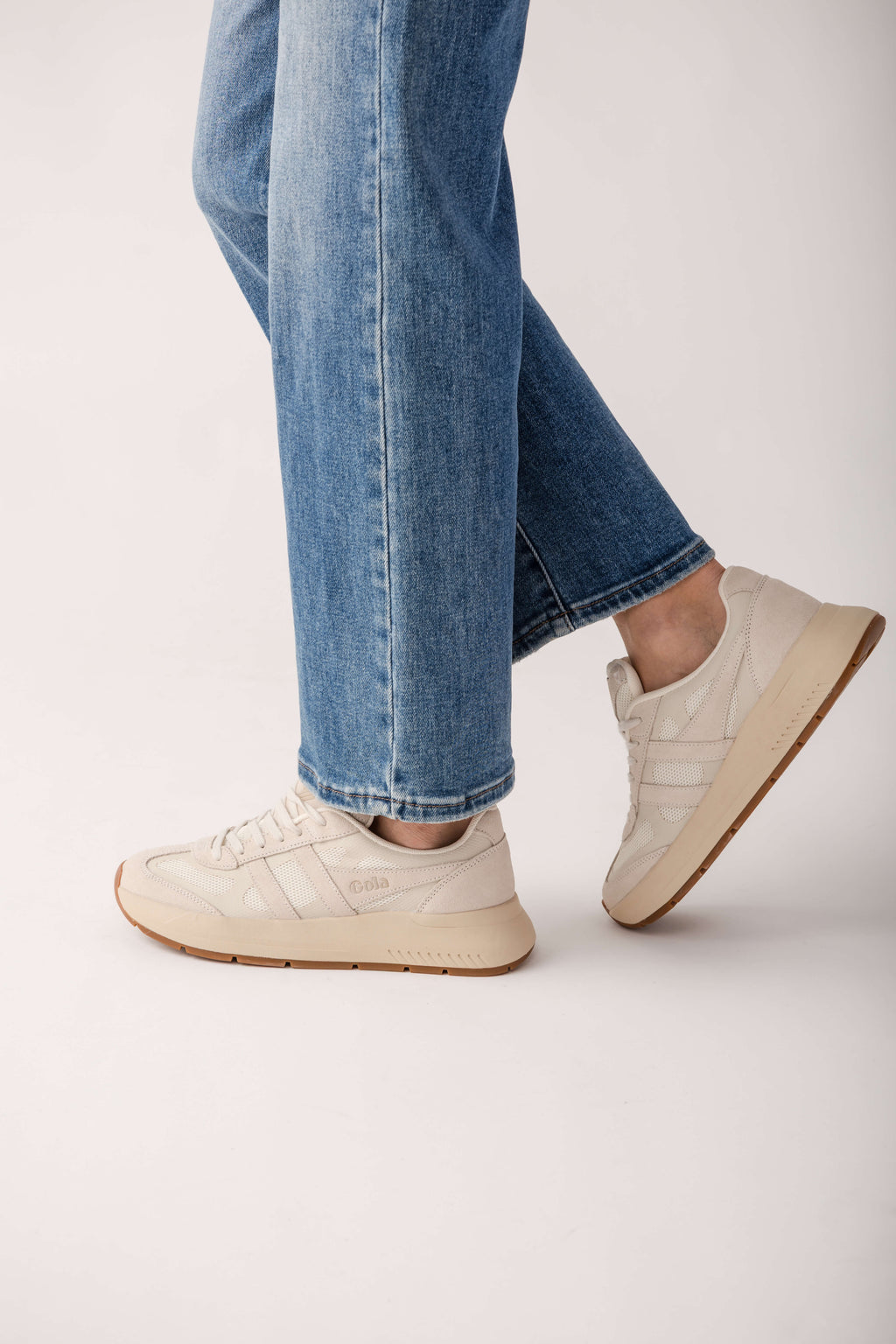 Cream-colored sneakers with lace-up closure and gum sole, worn with blue jeans.