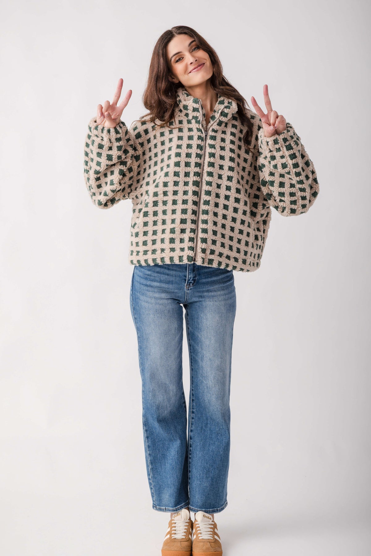 Woman wearing cream and green checkered sherpa fleece zip-up jacket with blue jeans and tan boots.