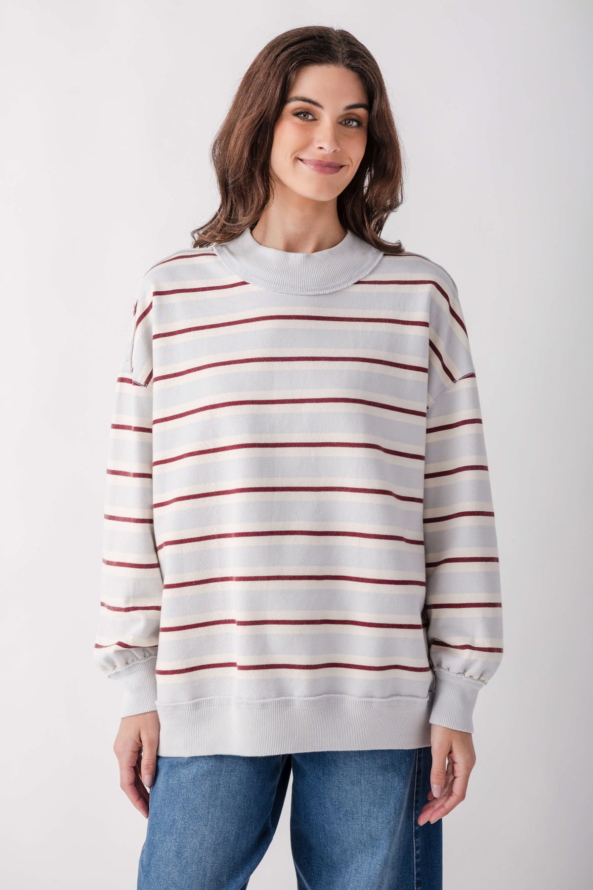 White and burgundy striped crewneck pullover with long sleeves worn with blue jeans.