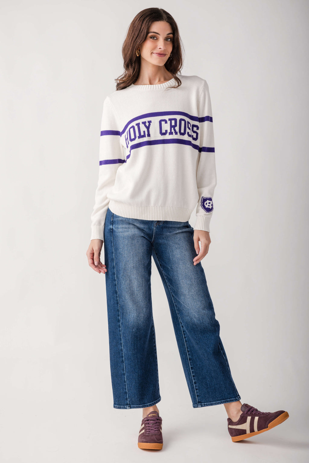 Cream crewneck sweater with navy "Holy Cross" text and stripes, paired with blue jeans.