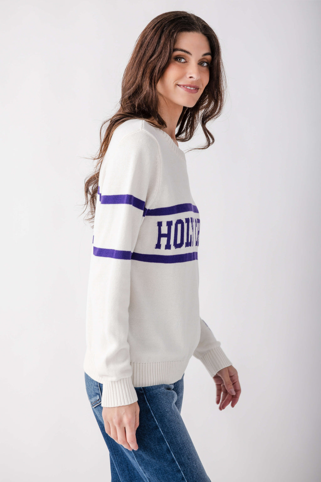 Cream knit sweater with navy stripes and "HOLLOWAY" text on chest, worn with blue jeans.