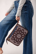 Brown bandana pouch with white floral and paisley pattern, brown leather handles, worn by person in jeans.