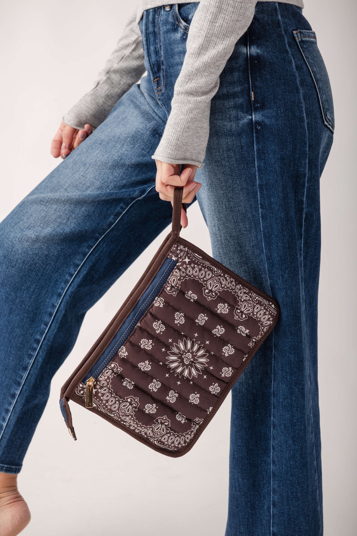 Brown bandana pouch with white floral and paisley pattern, brown leather handles, worn by person in jeans.