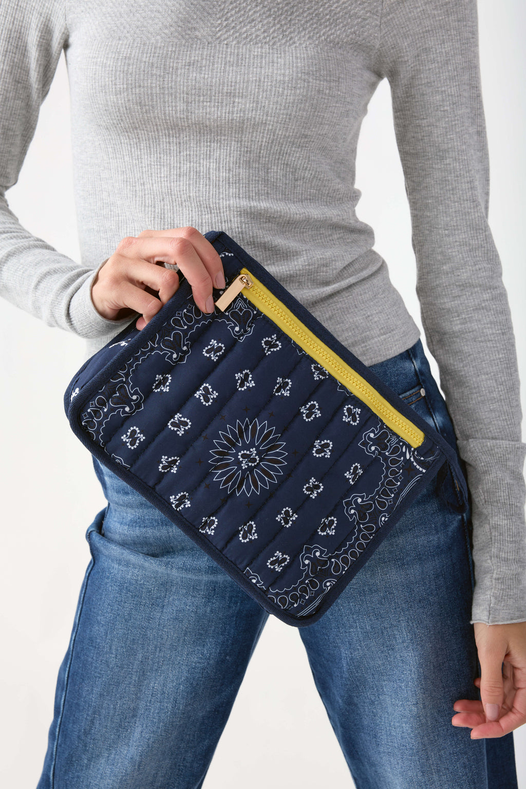 Navy bandana pouch with white sunflower and ornamental print, yellow zip closure, held against body.