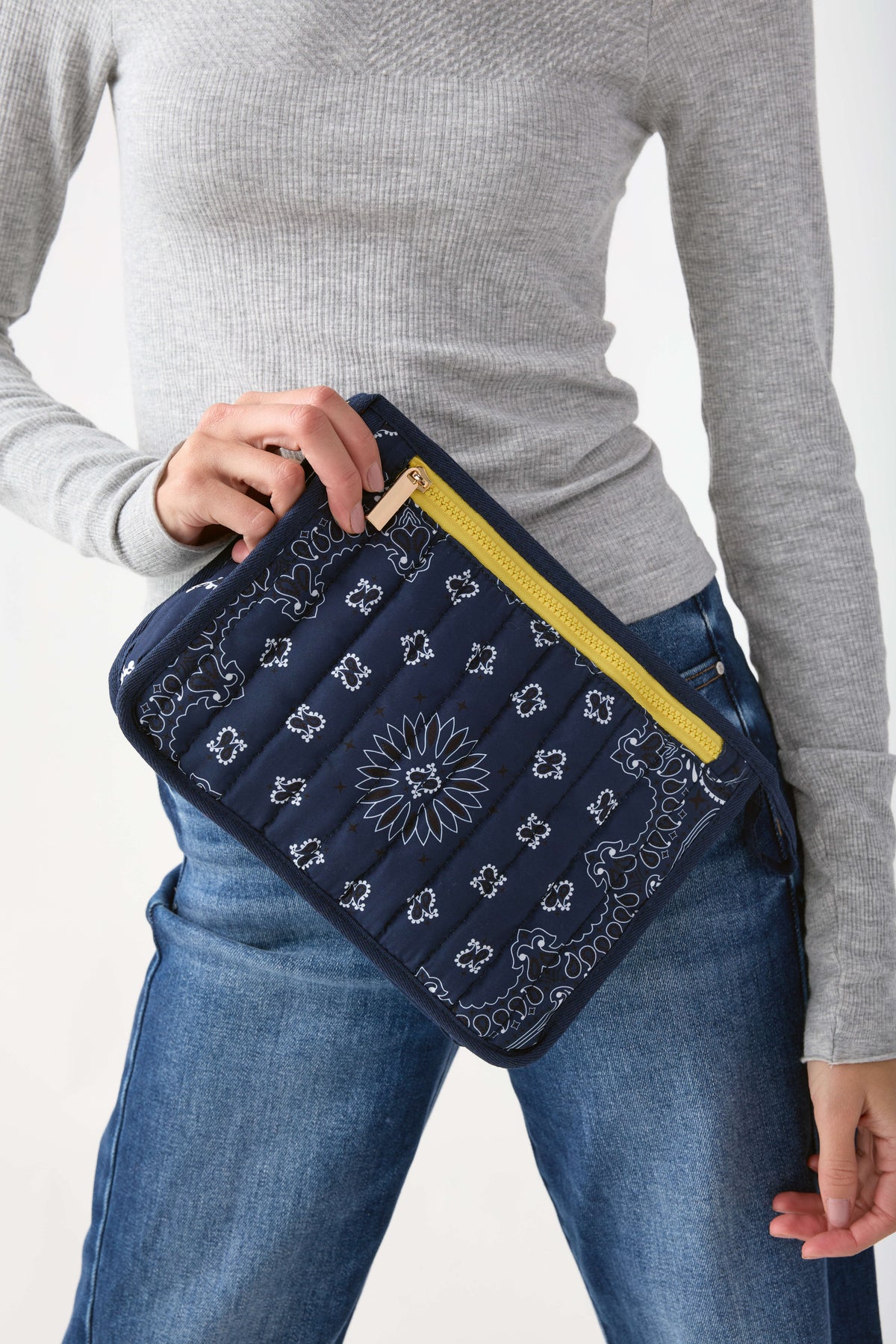 Navy bandana pouch with white sunflower and ornamental print, yellow zip closure, held against body.