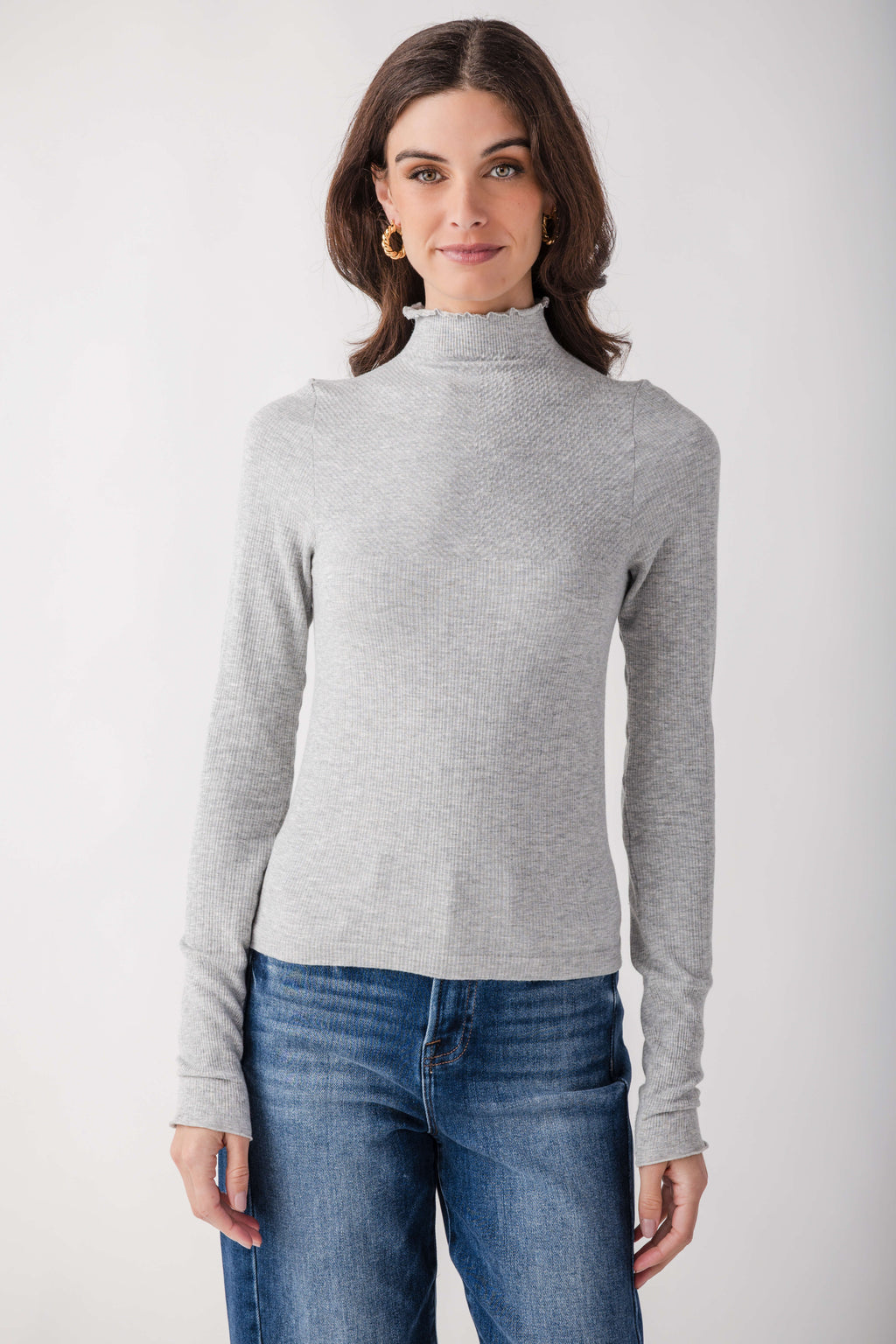 Light gray ribbed mock neck long-sleeve top with seamless construction worn with blue jeans.