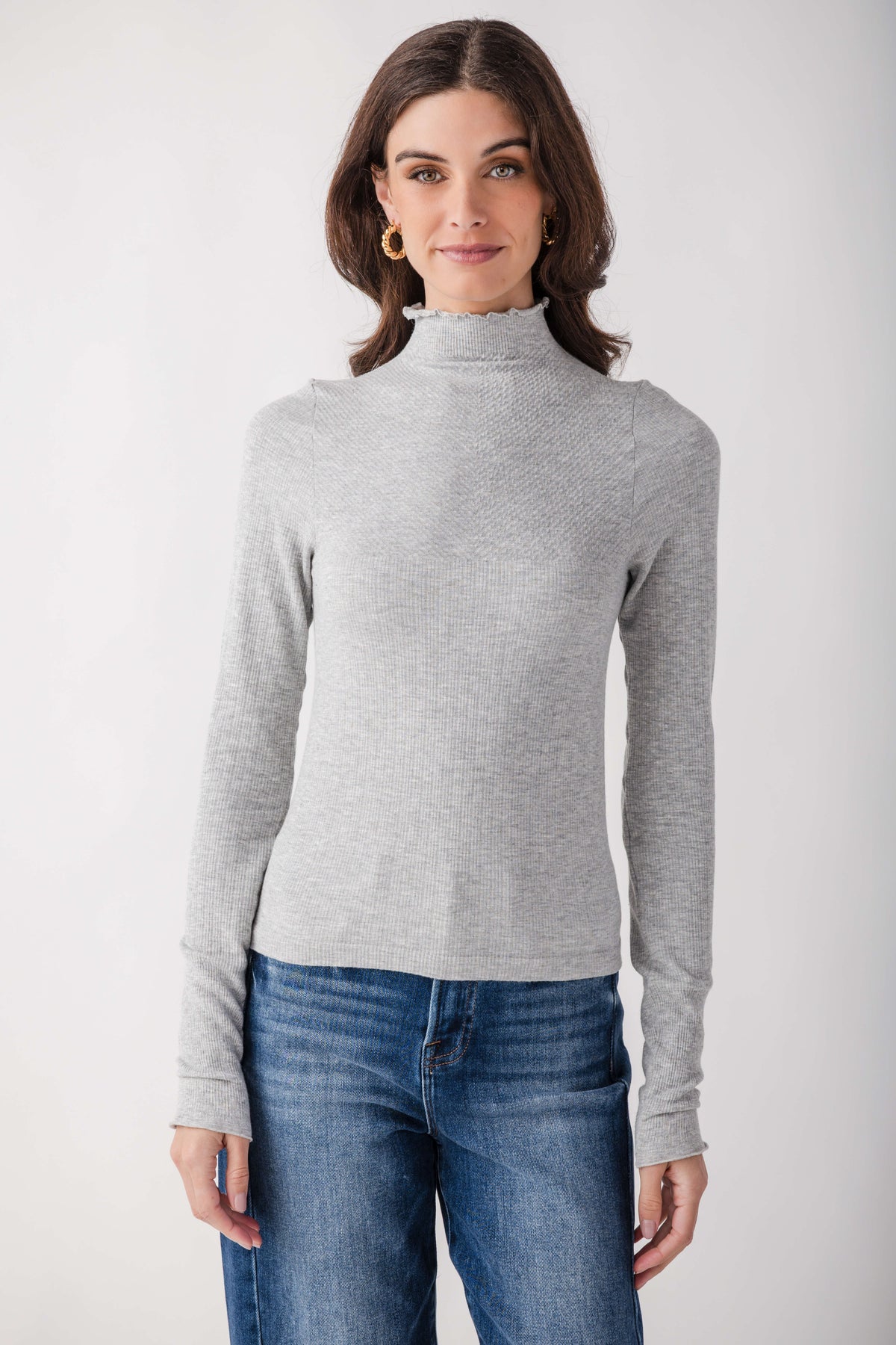 Light gray ribbed mock neck long-sleeve top with seamless construction worn with blue jeans.