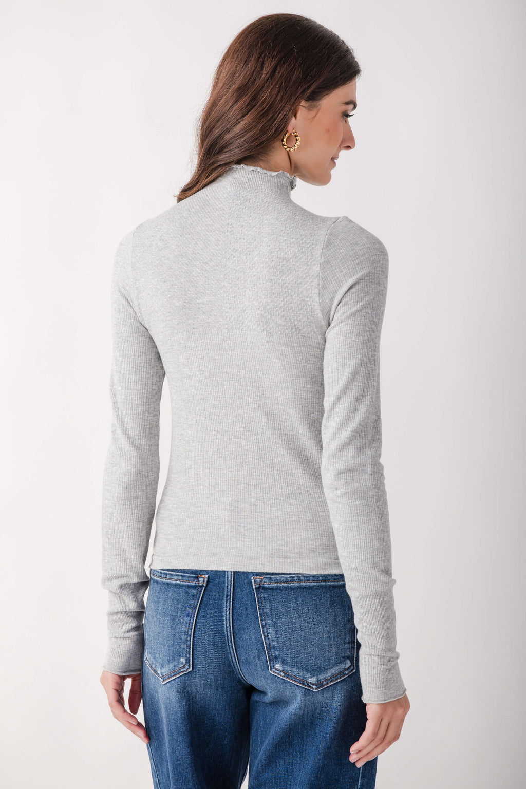 Light gray ribbed mock neck long-sleeve top worn with blue jeans, shown from back view.