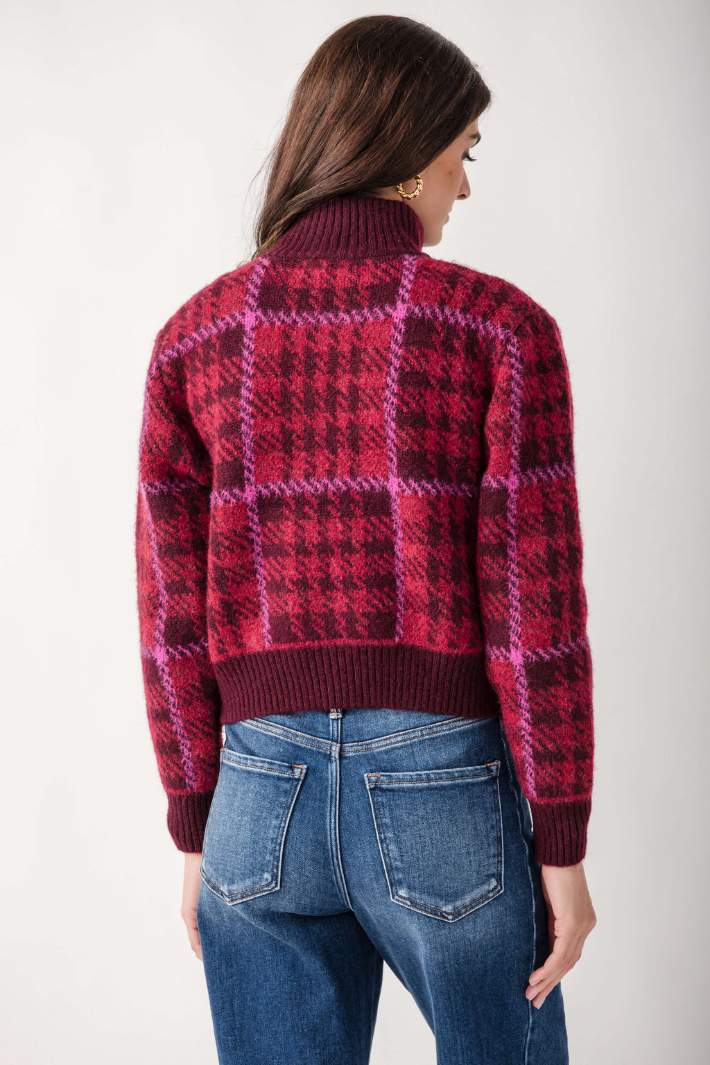 Woman wearing a pink and burgundy plaid mock neck jacket with a cropped fit, paired with blue jeans.