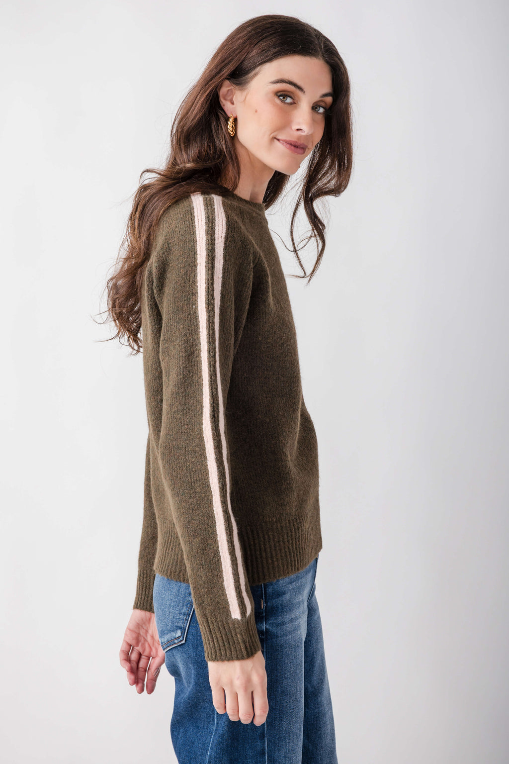 Olive knit sweater with white and brown contrast stripes running down the sleeves, worn with blue jeans.