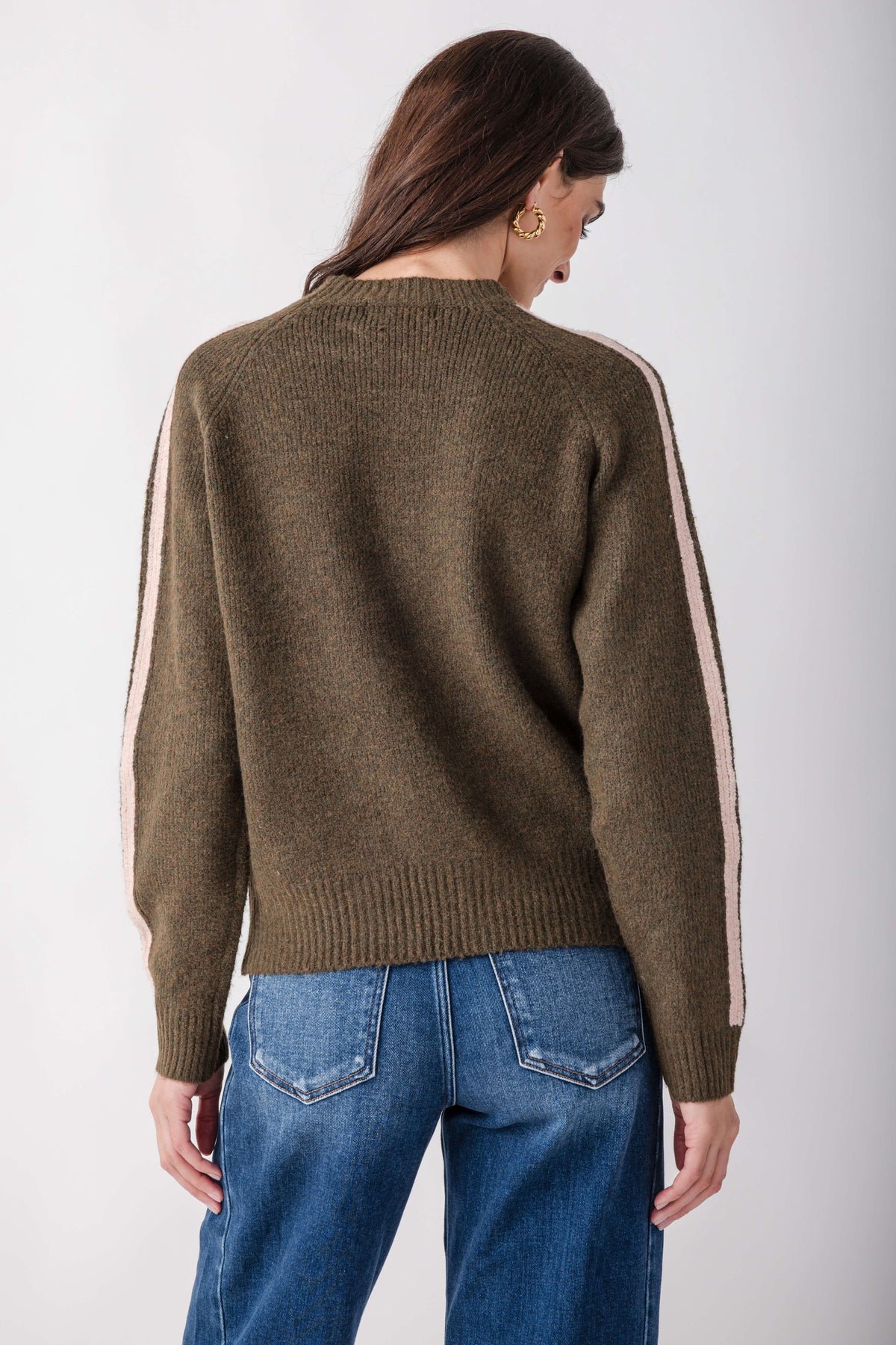 Olive knit sweater with pink and white contrast stripes running down the sleeves, worn with blue jeans.