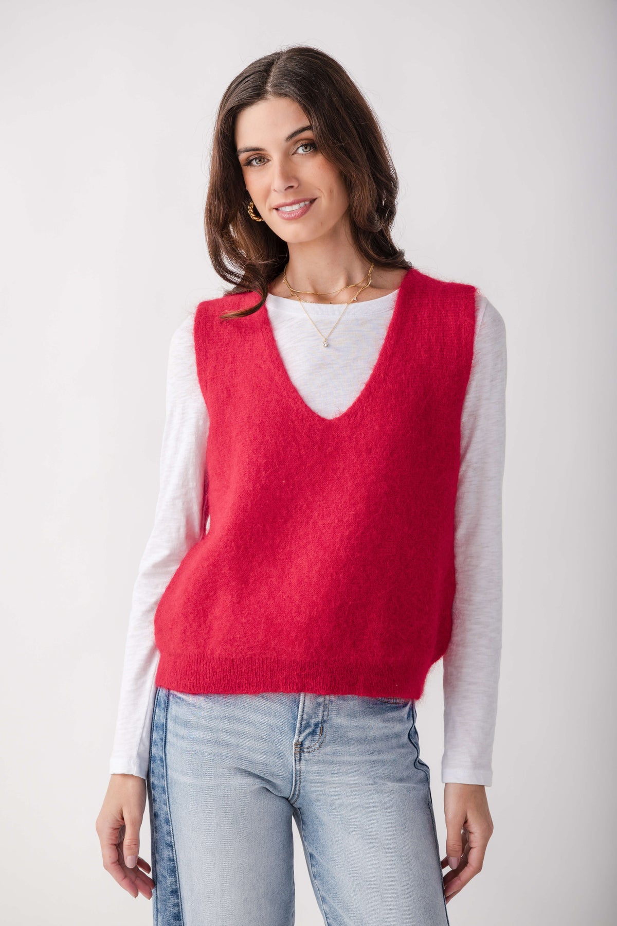 Red knit sweater vest with V-neck worn over white long-sleeve shirt, styled with light blue jeans.