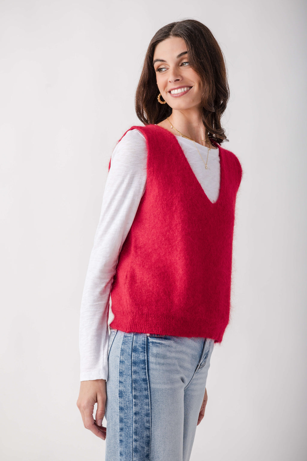 Red knit sweater vest with V-neckline layered over white long-sleeve top and light blue jeans.