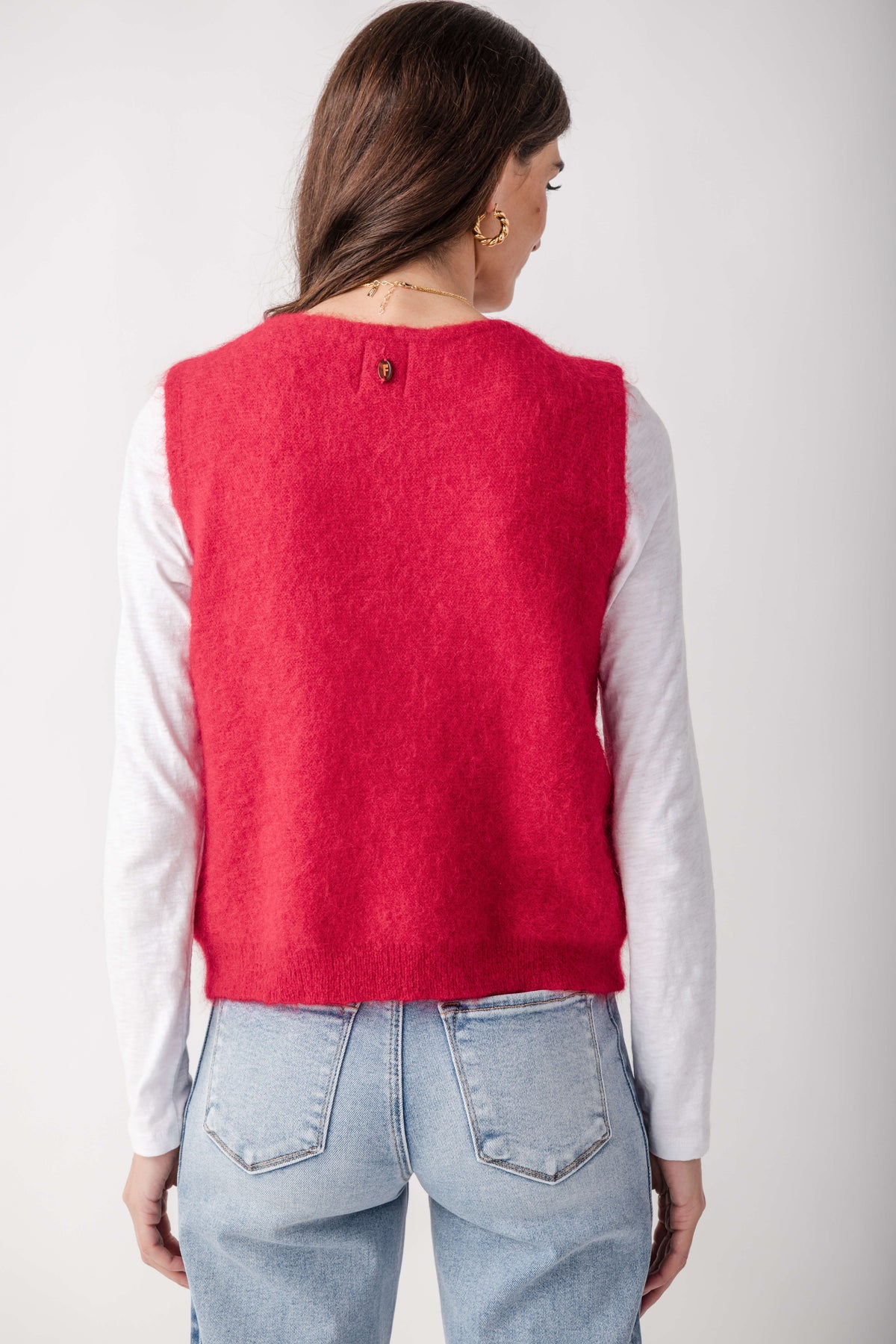 Red knit sweater vest worn over white long-sleeved shirt, paired with light blue jeans.