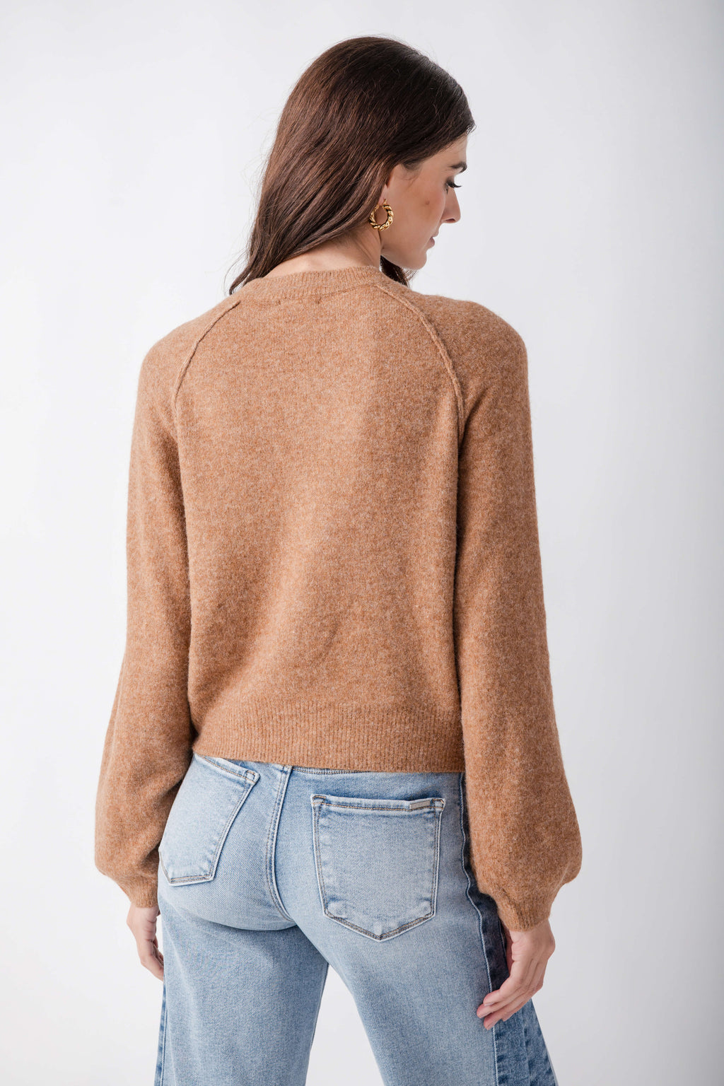 Woman wearing a tan knit henley sweater with long sleeves, shown from the back, paired with light blue jeans.