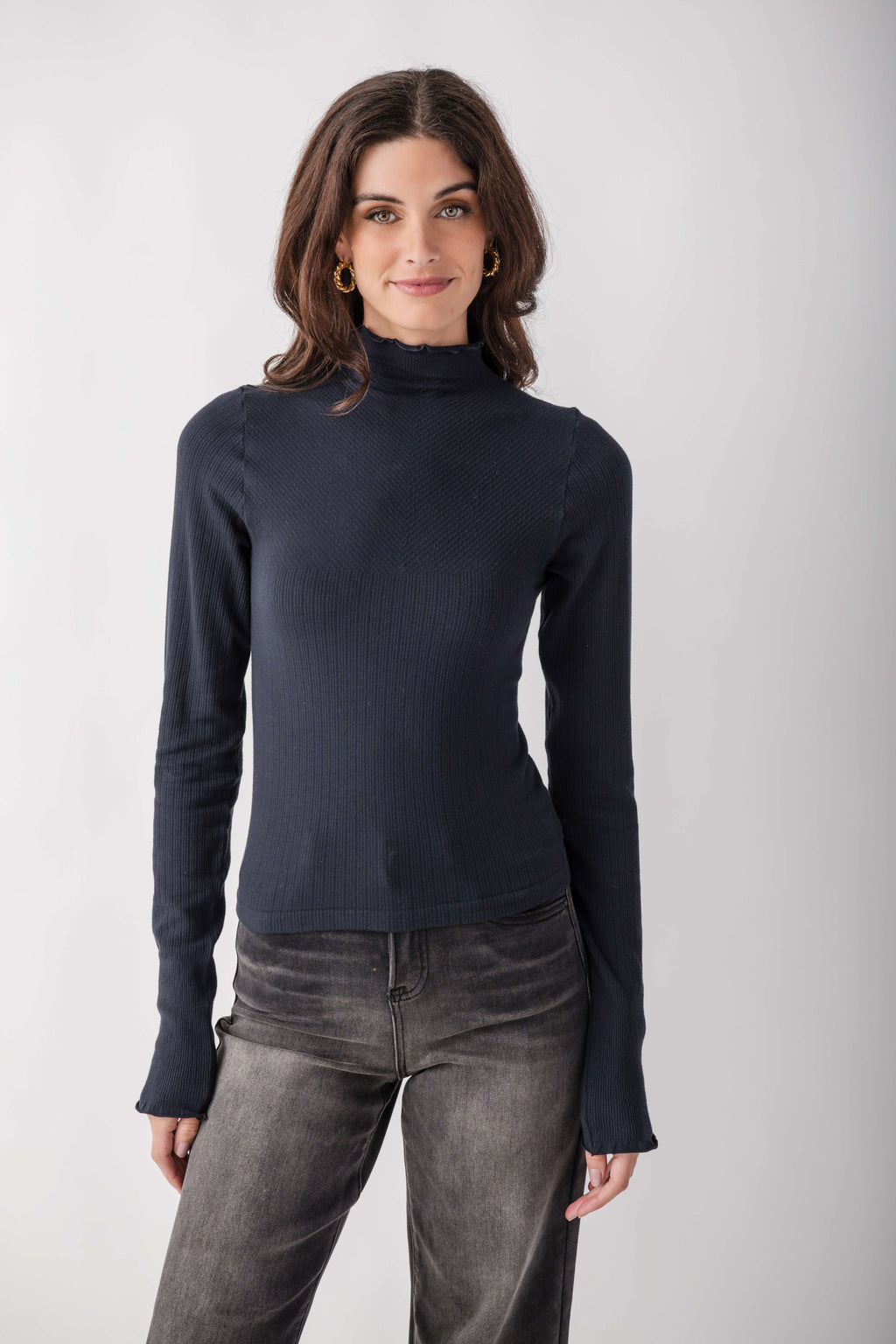 Woman wearing a dark navy ribbed mock neck long-sleeve top with gray jeans.