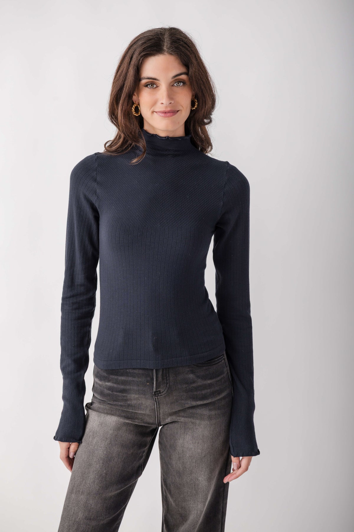 Woman wearing a dark navy ribbed mock neck long-sleeve top with gray jeans.