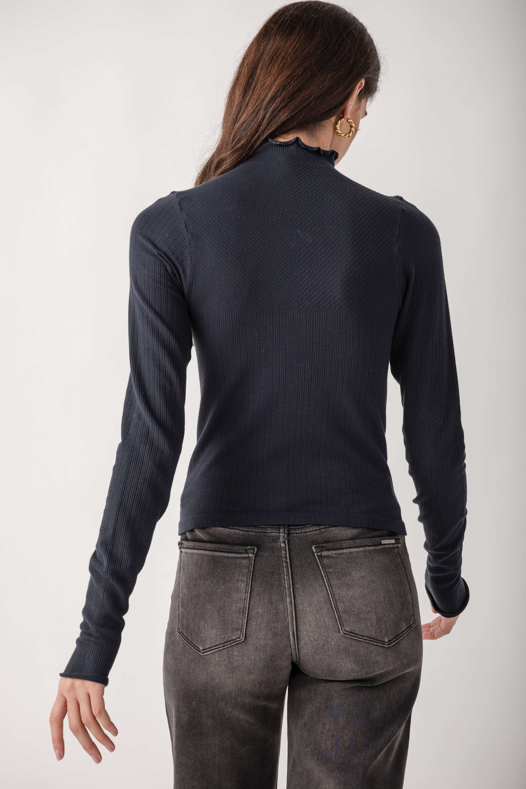 Woman wearing a dark navy ribbed mock neck long-sleeve top with gray denim jeans, shown from back view.