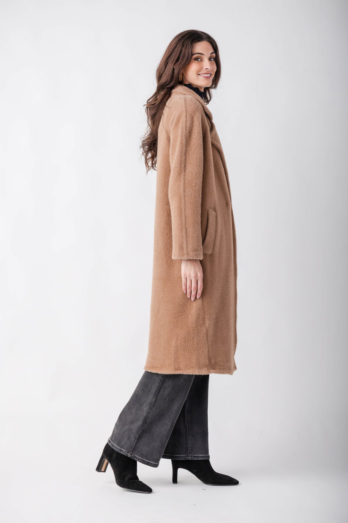 Woman wearing a tan cocoon coat over gray denim and black ankle boots, shown from the side.