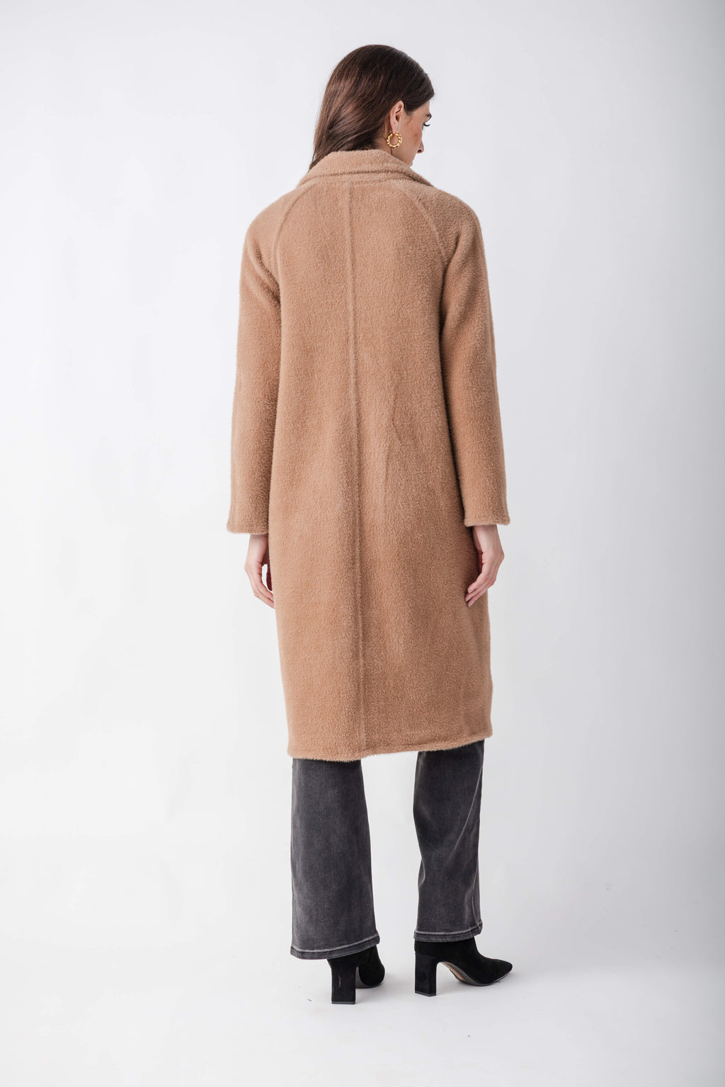 Woman wearing a beige cocoon coat with a collared neckline over dark jeans and black boots, viewed from behind.