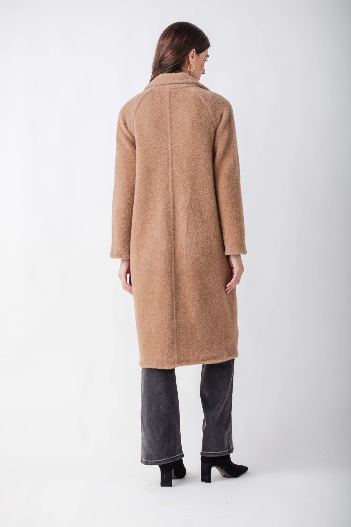 Woman wearing a beige cocoon coat with a collared neckline over dark jeans and black boots, viewed from behind.
