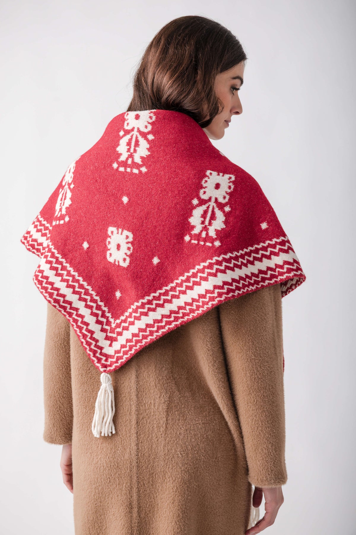 Red and white patterned knit shawl with geometric designs worn over a beige wool coat.