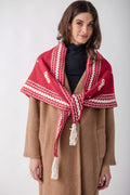 Red and white patterned knit shawl with tassels worn over a tan wool coat.