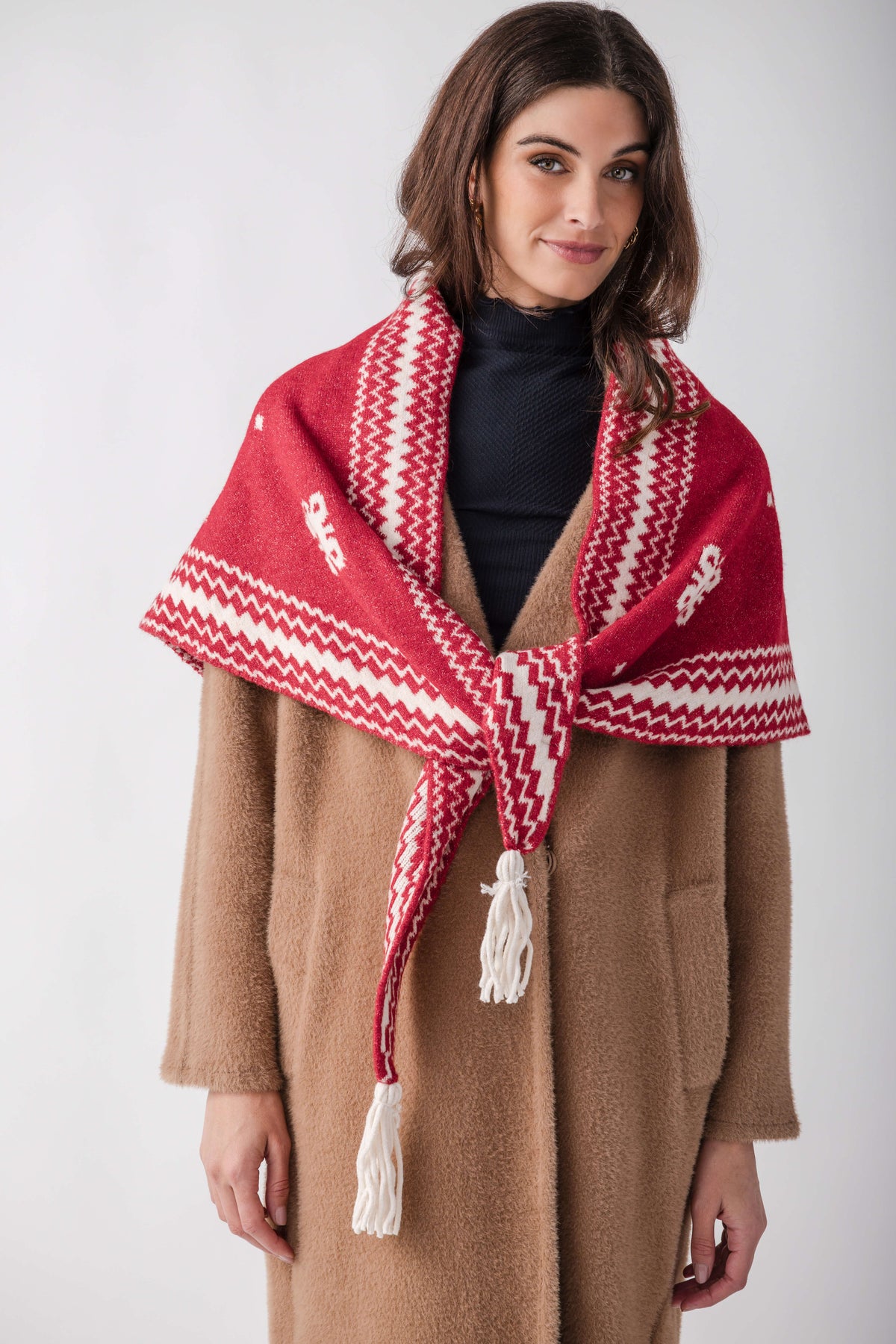 Red and white patterned knit shawl with tassels worn over a tan wool coat.