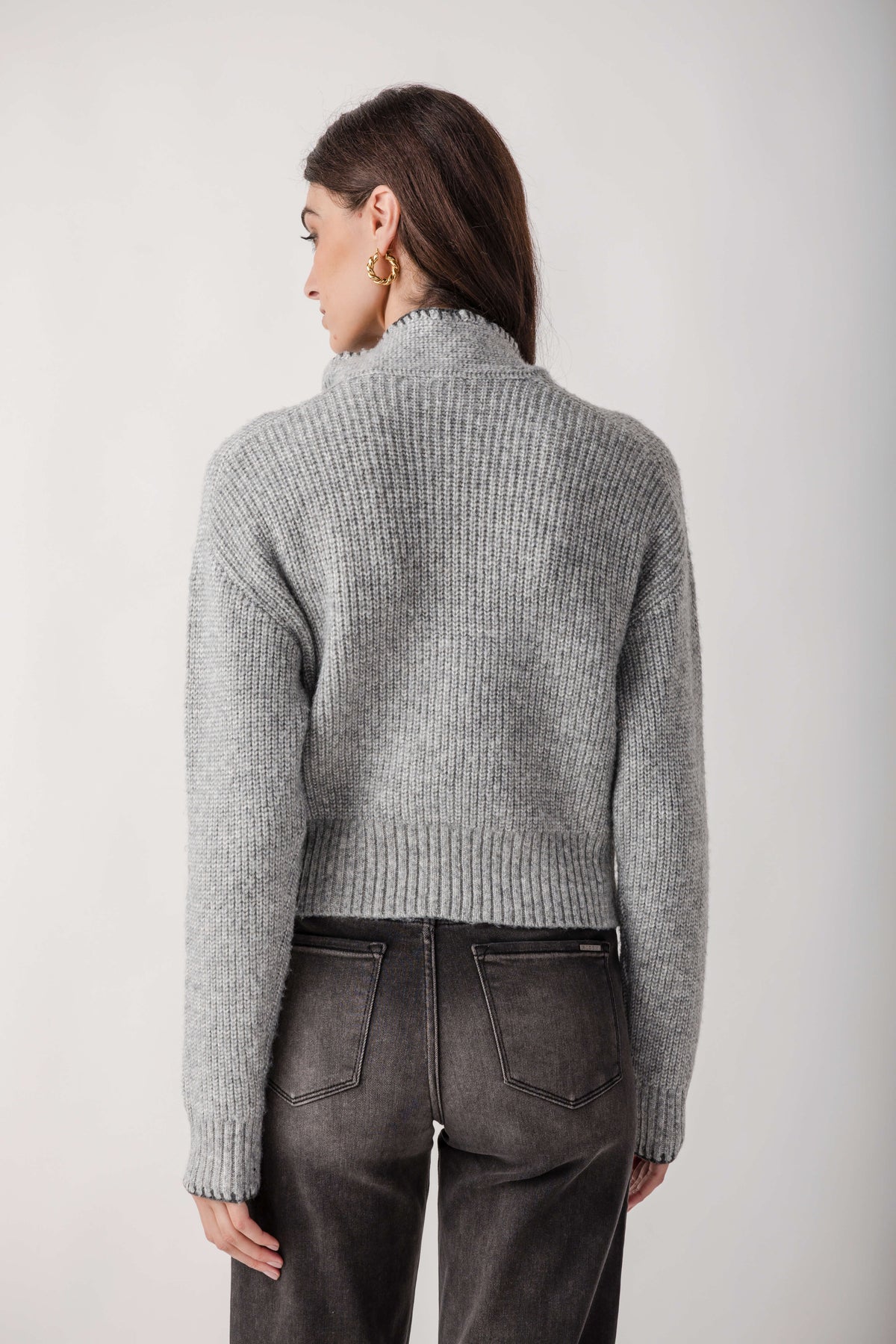 Gray ribbed turtleneck sweater with cropped silhouette worn with dark denim jeans, back view.