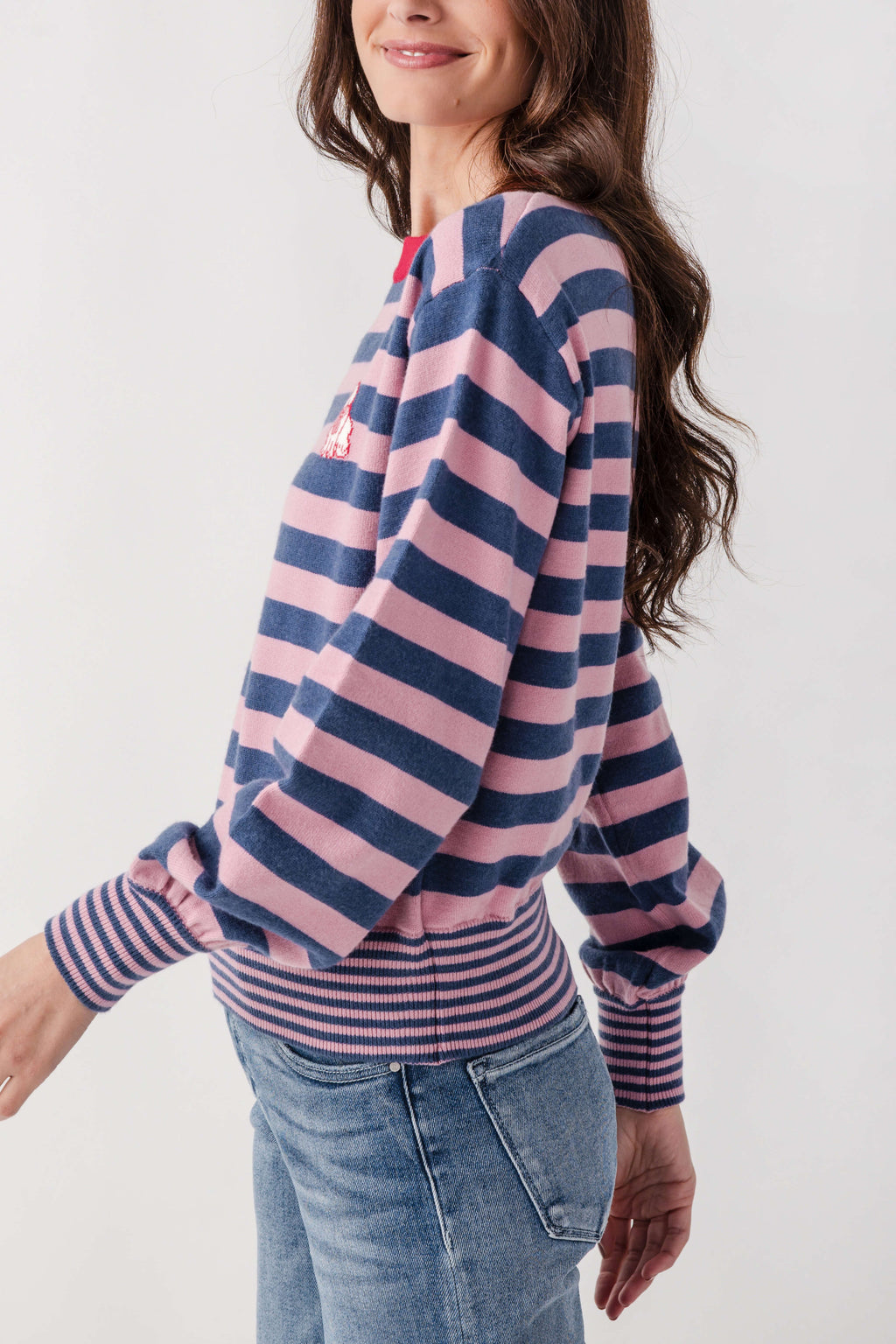 Woman wearing navy and pink striped sweater with ribbed cuffs and small embroidered dog detail on sleeve.