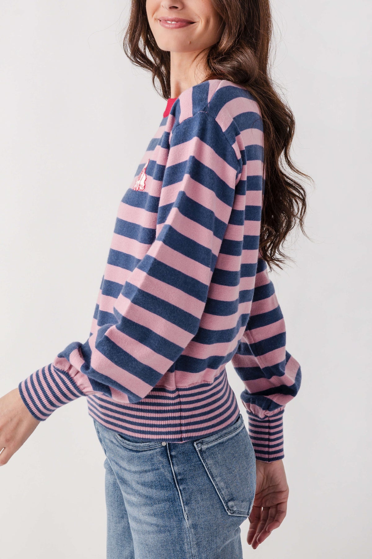 Woman wearing navy and pink striped sweater with ribbed cuffs and small embroidered dog detail on sleeve.