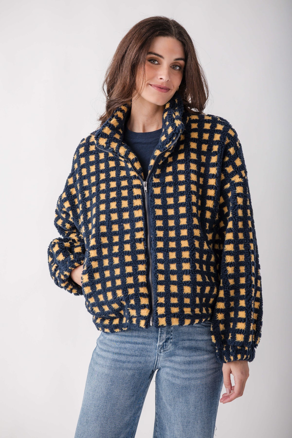 Woman wearing a navy and gold checkered sherpa fleece jacket with a full-length zipper over a dark shirt and light blue jeans