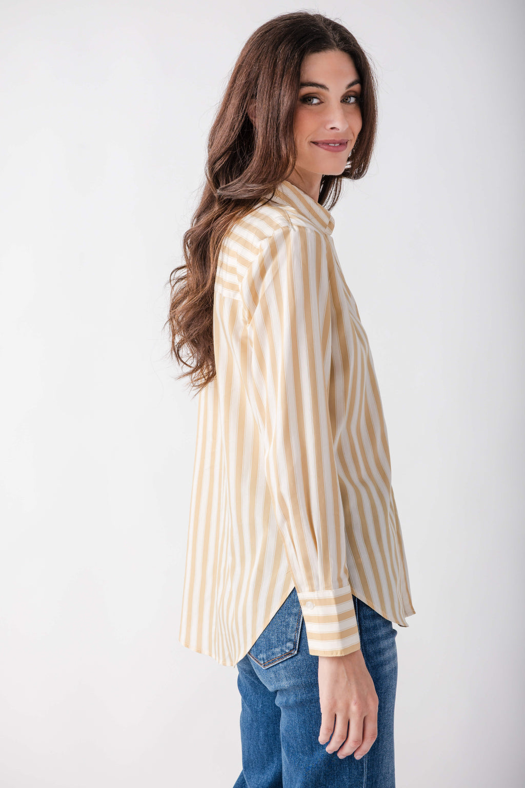 Tan and white striped button-up shirt worn over blue jeans, shown from the side on a model.