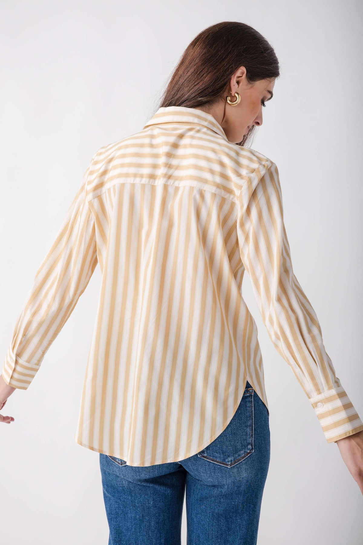 Golden and white striped button-up shirt with long sleeves worn with blue jeans.