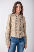 A woman modeling a cropped, long-sleeve jacket with a beige and brown floral pattern, paired with blue jeans, against a light gray studio background.
