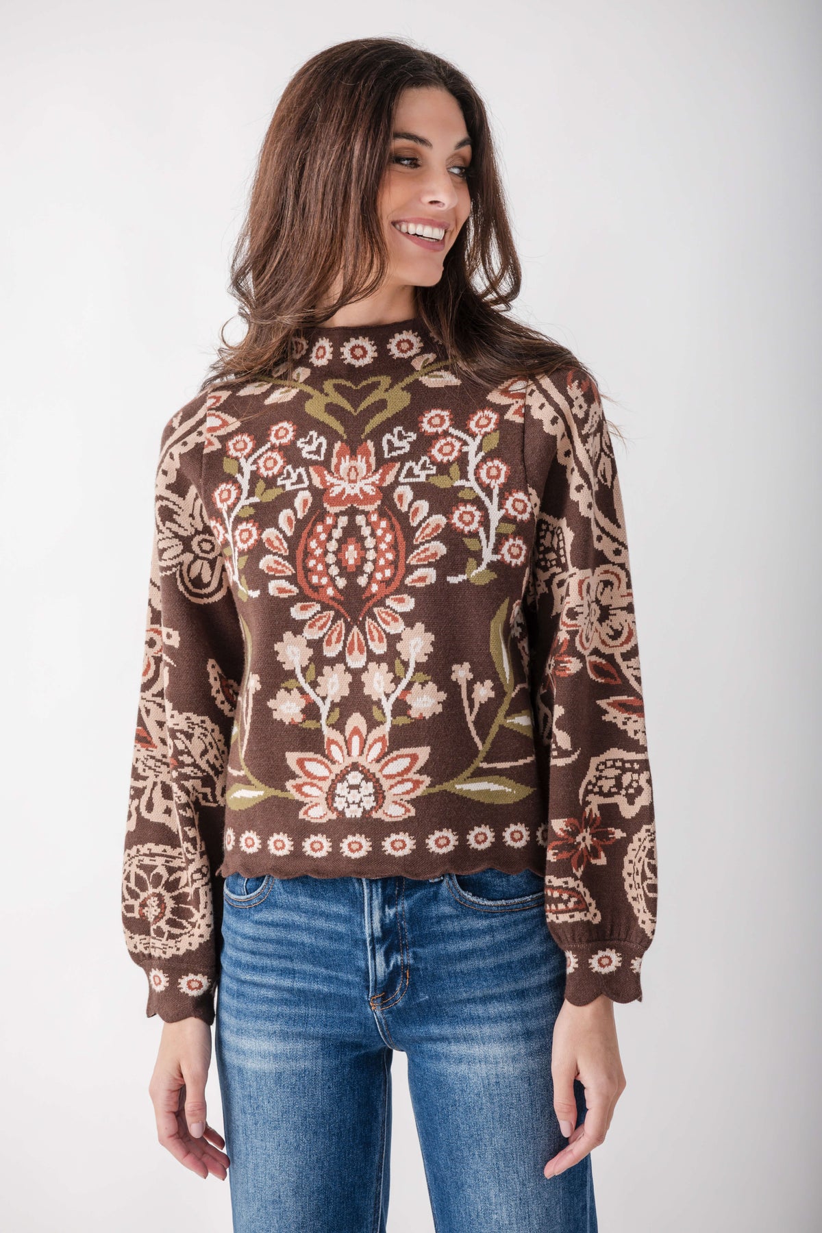 Brown sweater with red, cream, and olive floral and geometric print, scalloped hem, long sleeves.