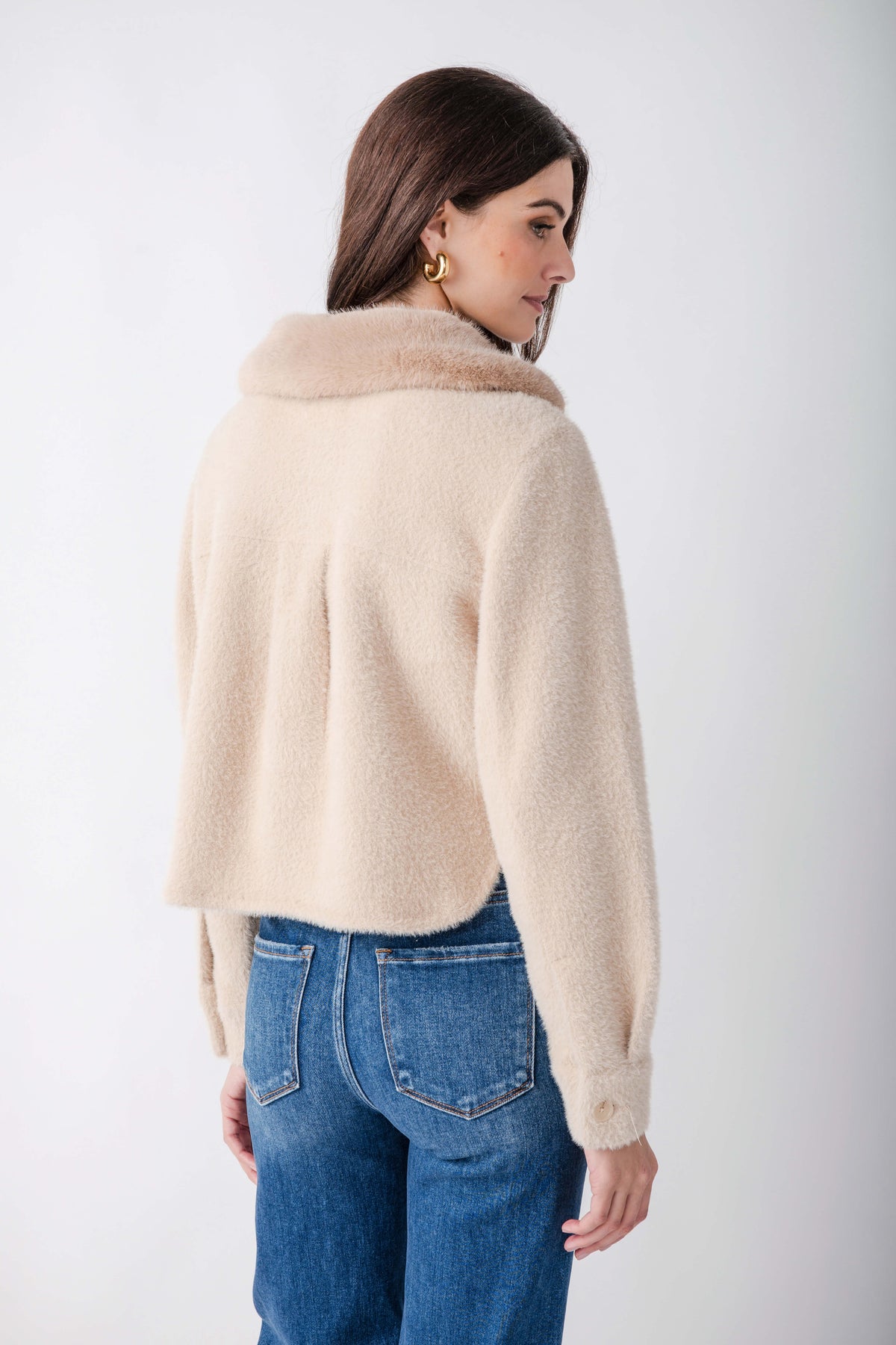 Cream-colored fuzzy jacket with cowl neckline worn over blue jeans, shown from back view.