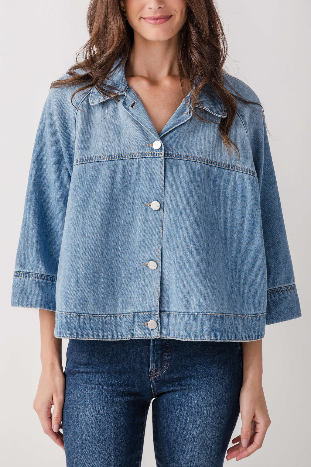 Light blue denim cropped cape jacket with white button closures and collar, worn over dark jeans.