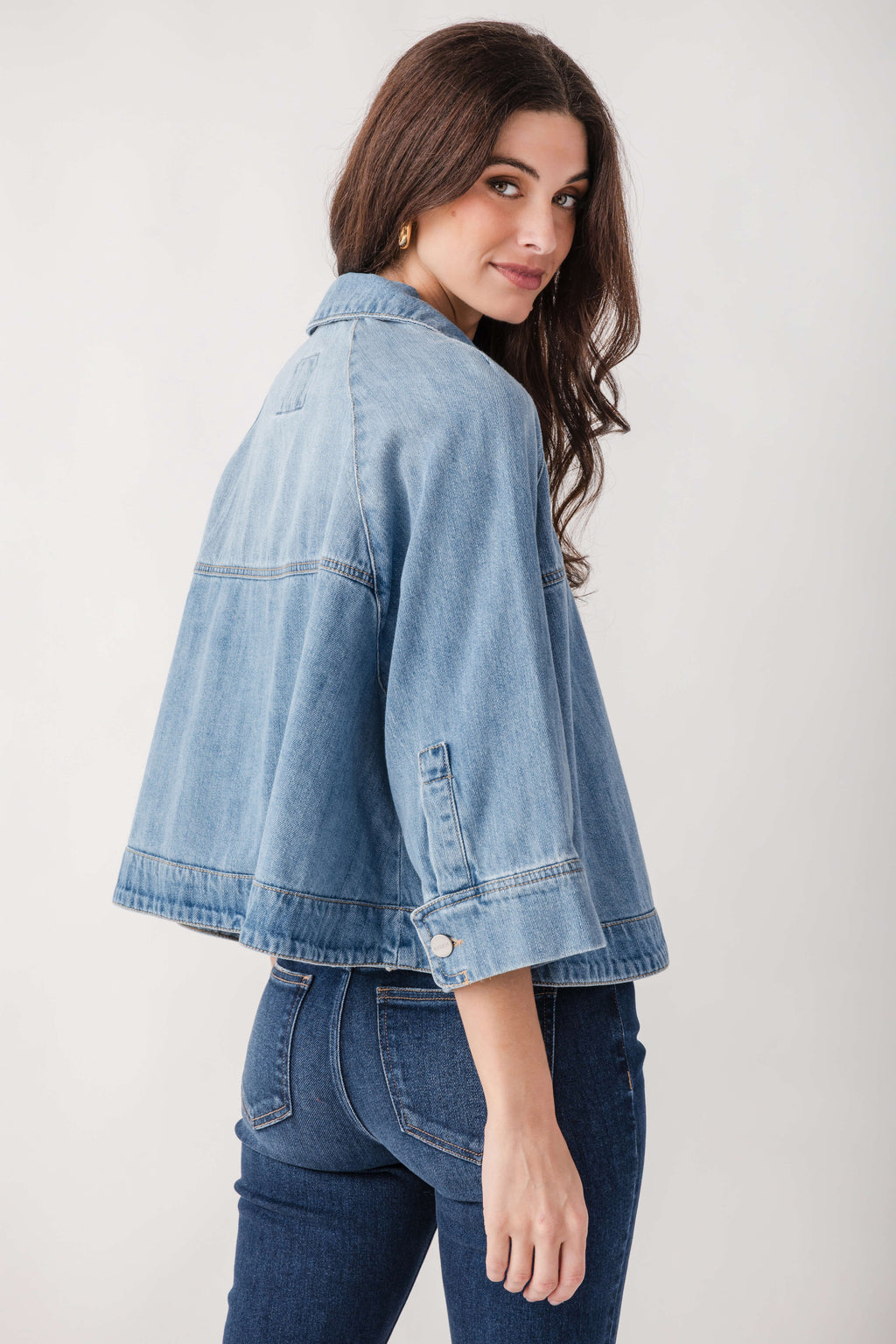 Light blue denim cropped cape jacket with collar and button front, worn over dark denim jeans.