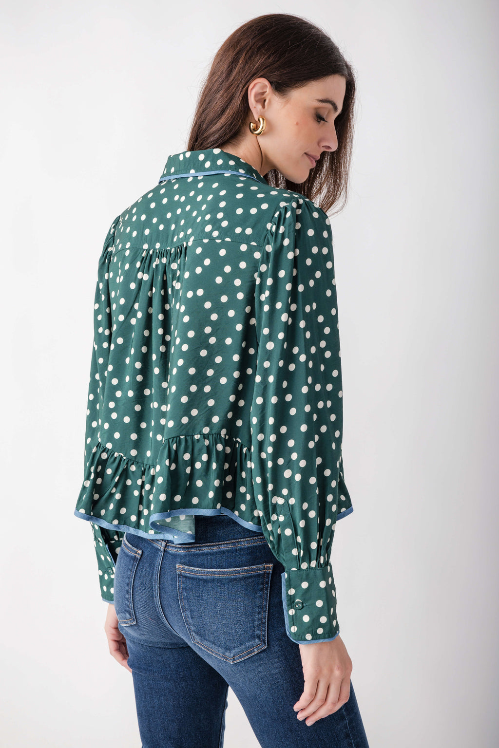 Woman wearing teal button-up blouse with white polka dots, Peter Pan collar, and ruffled hem details.