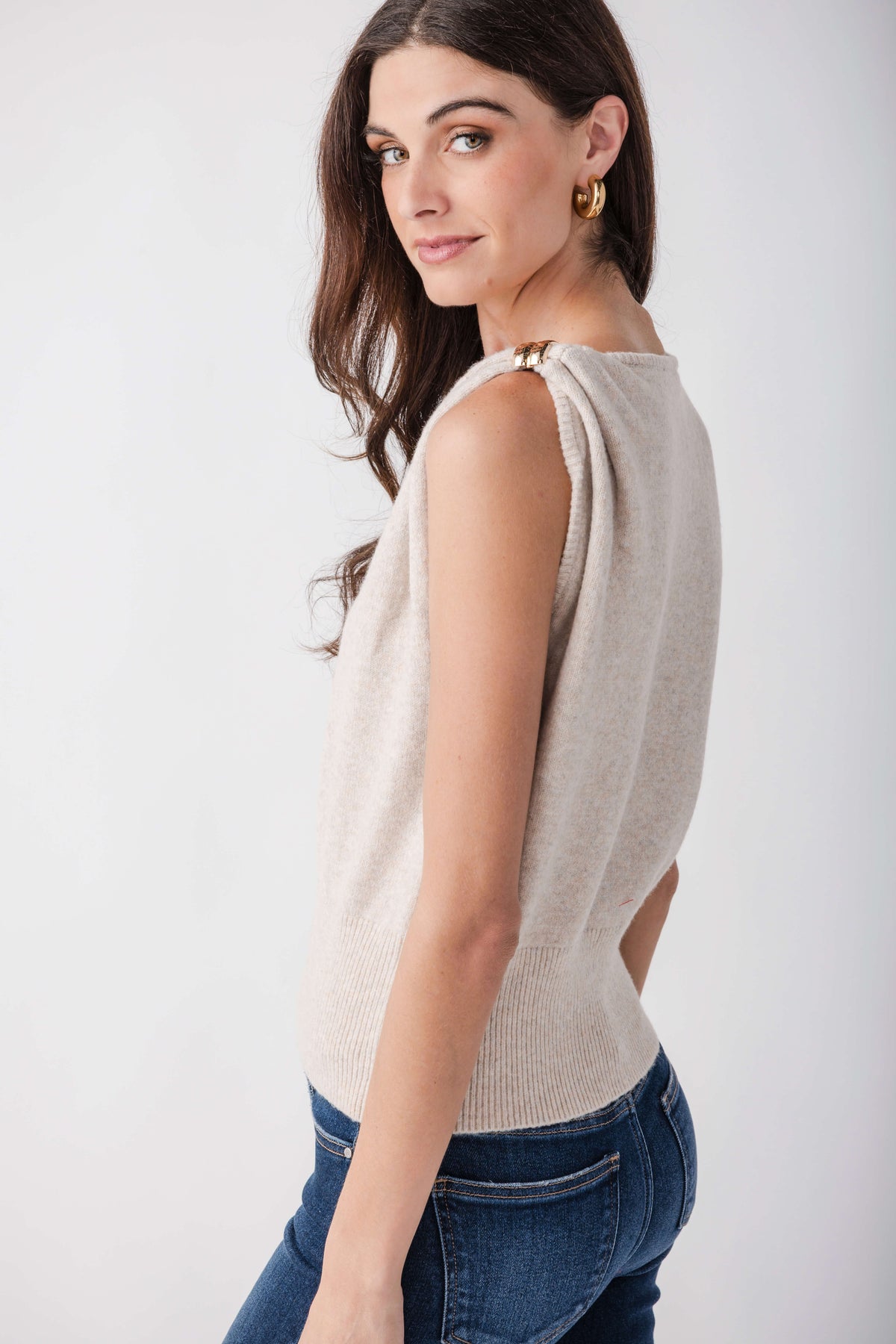 Beige sleeveless knit top with gold brooch detail at shoulder, worn with blue jeans.