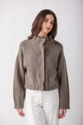 Taupe knit jacket with pleated ruffle detail at center front and cuffs, cropped length, worn with white pants.