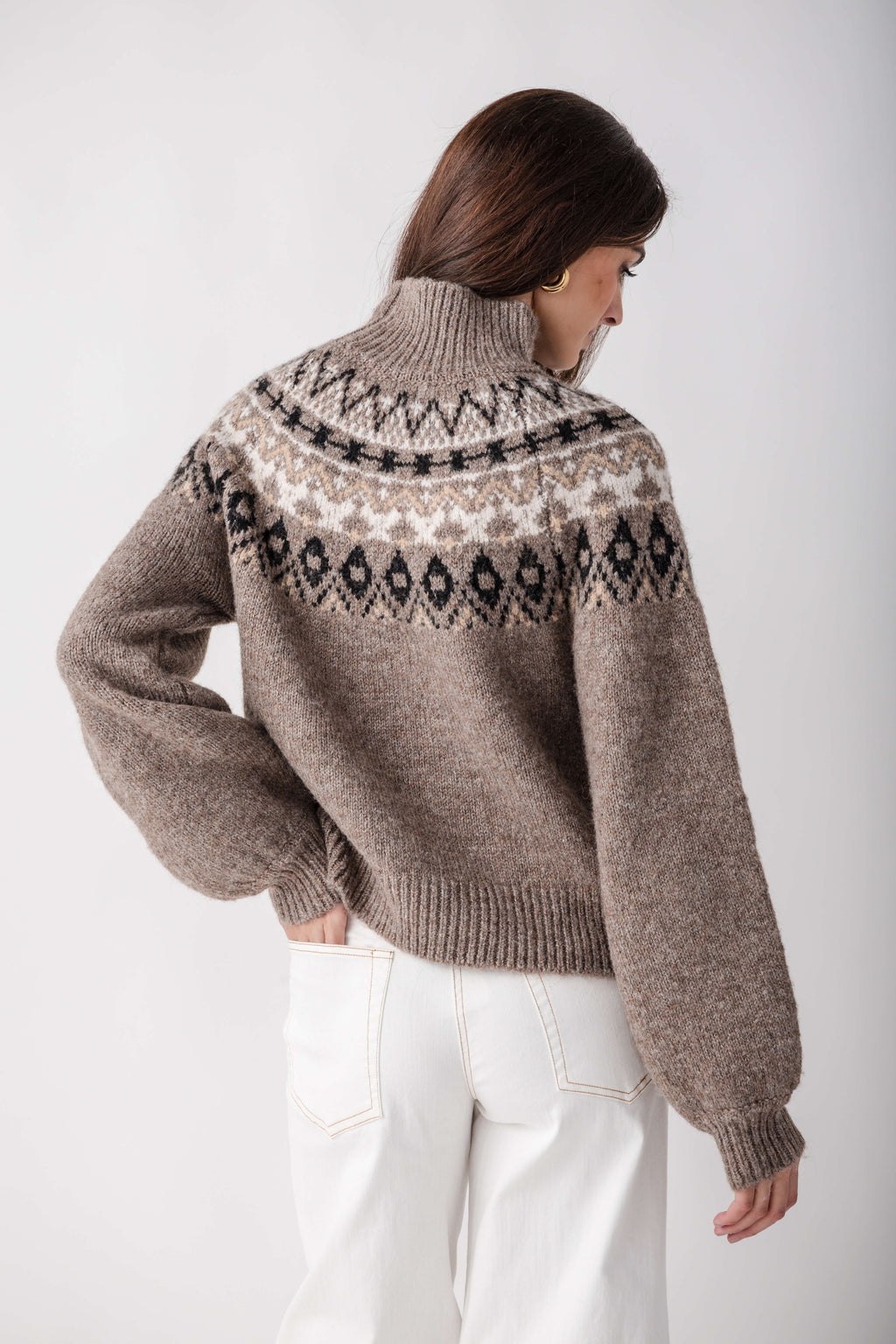 Beige turtleneck sweater with black and cream geometric pattern on yoke, worn with white jeans.
