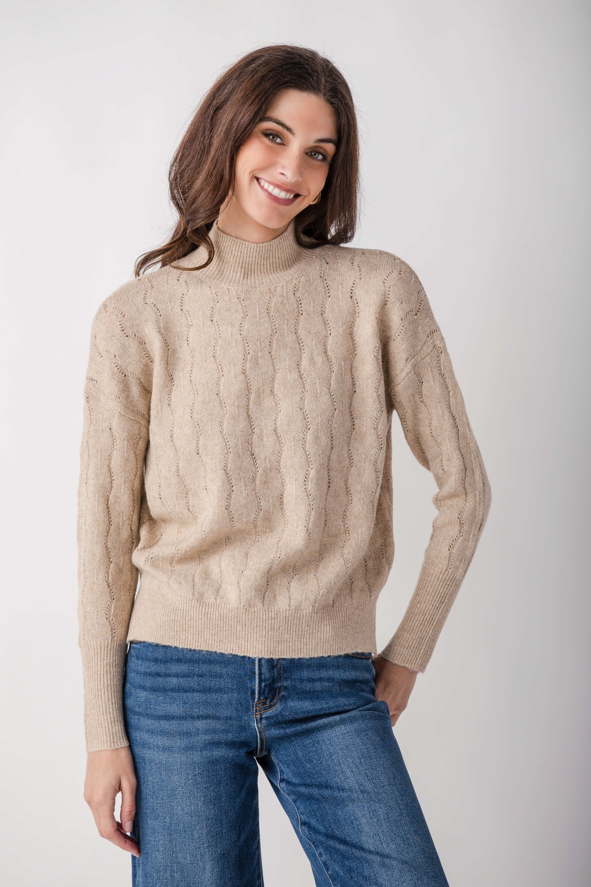 Beige turtleneck sweater with lurex shimmer and cable knit pattern on model wearing jeans.